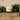 Candle in a glass jar with a label on a wooden surface with greenery in the background