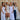 Five women posing together outdoors against a wooden fence, wearing white and light-colored clothing.