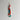 A pair of handmade beaded drop earrings hanging from a metal hook against a plain light gray wall. The earrings feature coral-red cylindrical beads, turquoise blue round beads, white marbled beads, and a small silver-toned metal clasp at the top.