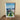 Framed cityscape print on a wooden surface with a neutral wall background