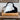 Black and white handbag on a wooden stool with a framed painting of a landscape in the background.