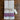 A folded white linen kitchen towel with red and blue stripes near the bottom, tied with twine and a handwritten paper tag, placed on a dark wooden surface.