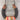 A handmade horseshoe-shaped necklace featuring dark gray wrapped metal, natural brown rusted ends, and a vibrant multicolor braided yarn fringe at the bottom, displayed on a gray wood background.