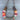 A rustic horseshoe-shaped necklace or wall hanging made from weathered metal, wrapped with multicolored yarn in pink, orange, white, and teal, and finished with a gray fur-like band, shown on a gray wood plank background.